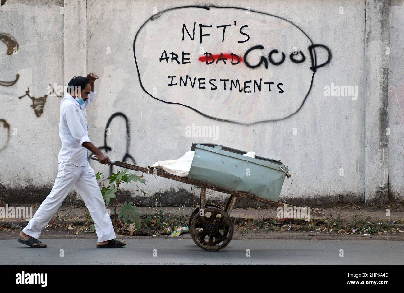 Mumbai, Indien. 18th. Februar 2022. Ein Schrotthändler mit einer schützenden Gesichtsmaske schiebt seinen Handwagen an einem Graffiti vorbei, das auf einer Wand mit der Aufschrift „NFT's are Good Investments“ in Mumbai gemalt ist.Non fungible Tokens (NFT) sind digitale Vermögenswerte, die reale Objekte wie Kunst, Musik, Fotos usw. Es ermöglicht dem Käufer, den Originalartikel mit digitalen Rechten zu besitzen. (Foto von Ashish Vaishnav/SOPA Images/Sipa USA) Quelle: SIPA USA/Alamy Live News Stockfoto