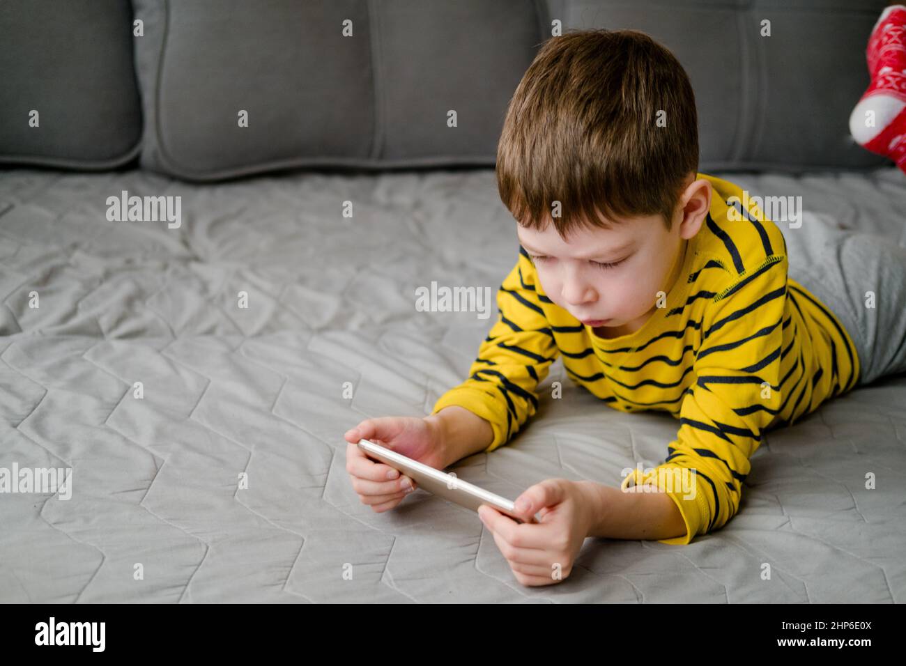 Ein Teenager liegt mit einem Telefon in den Händen auf der Couch. Das Kind spielt zu Hause am Telefon. Erholung mit dem Telefon. Urlaub mit Gadgets. Stockfoto