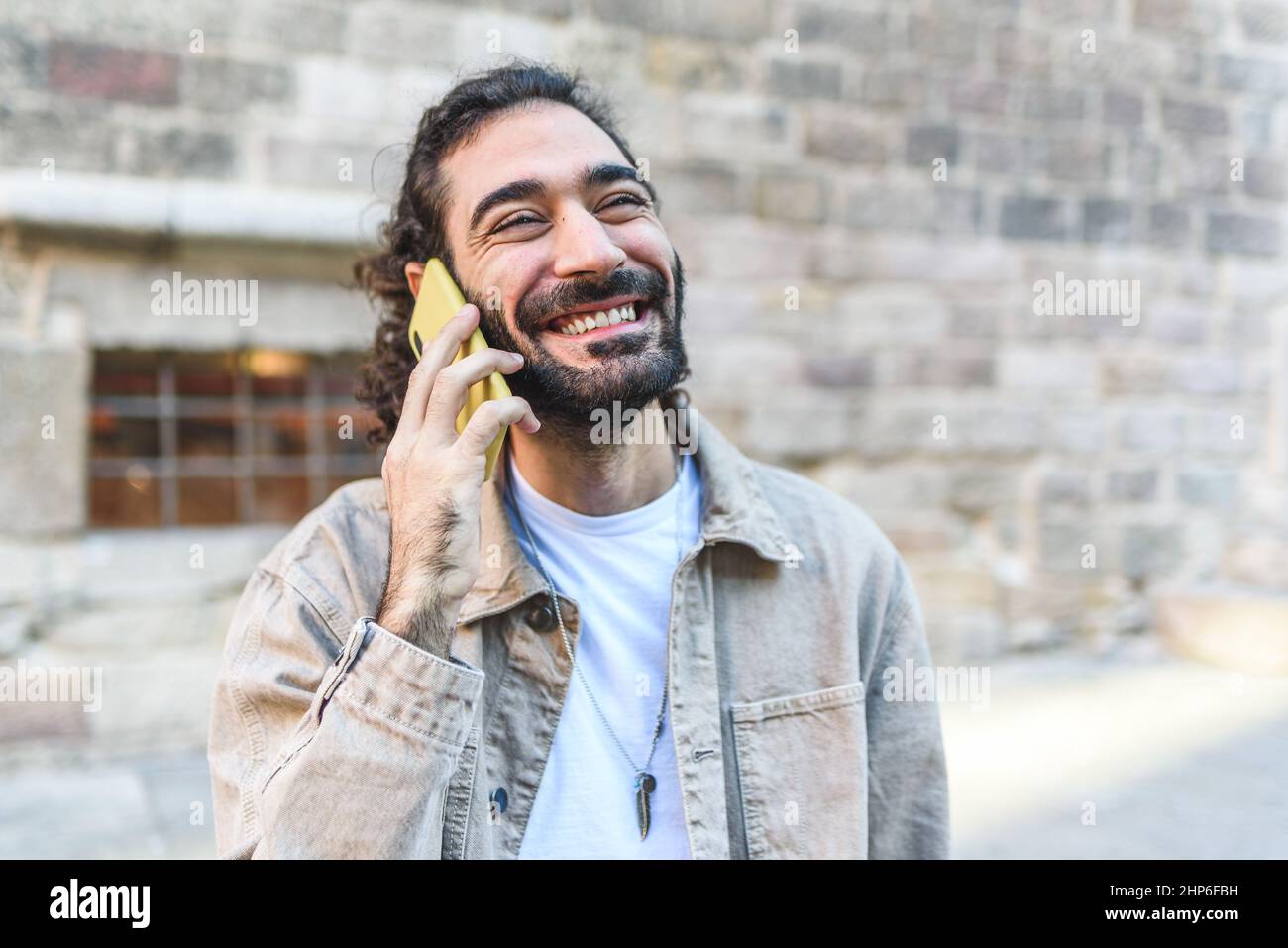 Entzückter bärtiger männlicher Tourist mit dunklem Haar, der sich auf dem Smartphone untersprach, während er in der Nähe eines alten Steingebäudes auf der Straße der Stadt stand Stockfoto