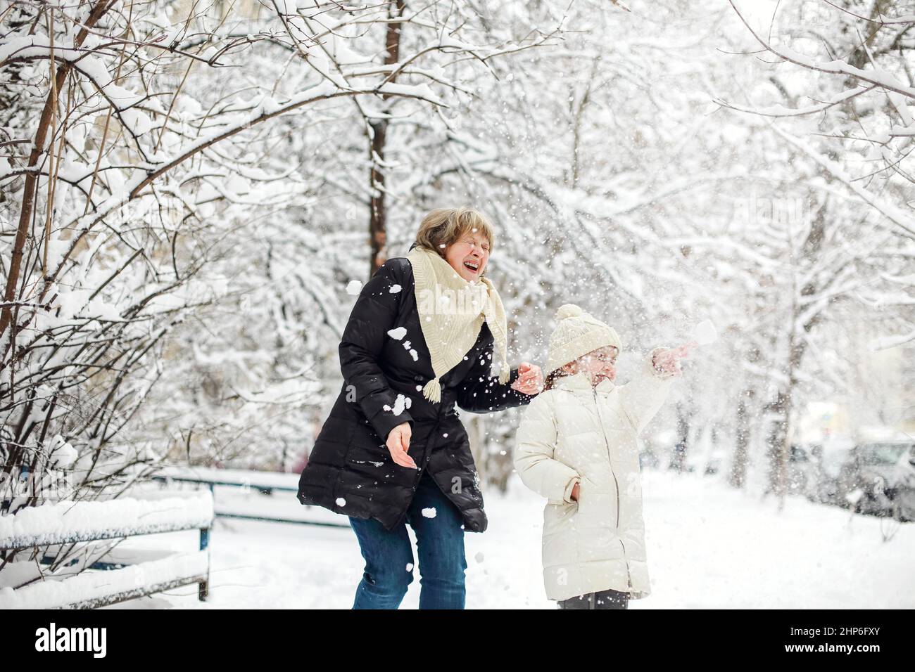 Fröhliche Familiengroßmutter mit Enkeln in warmer Kleidung, die im Winterpark spielen, frostiges und schneebedecktes Wetter genießen, die Kinder spucken aktiv Stockfoto