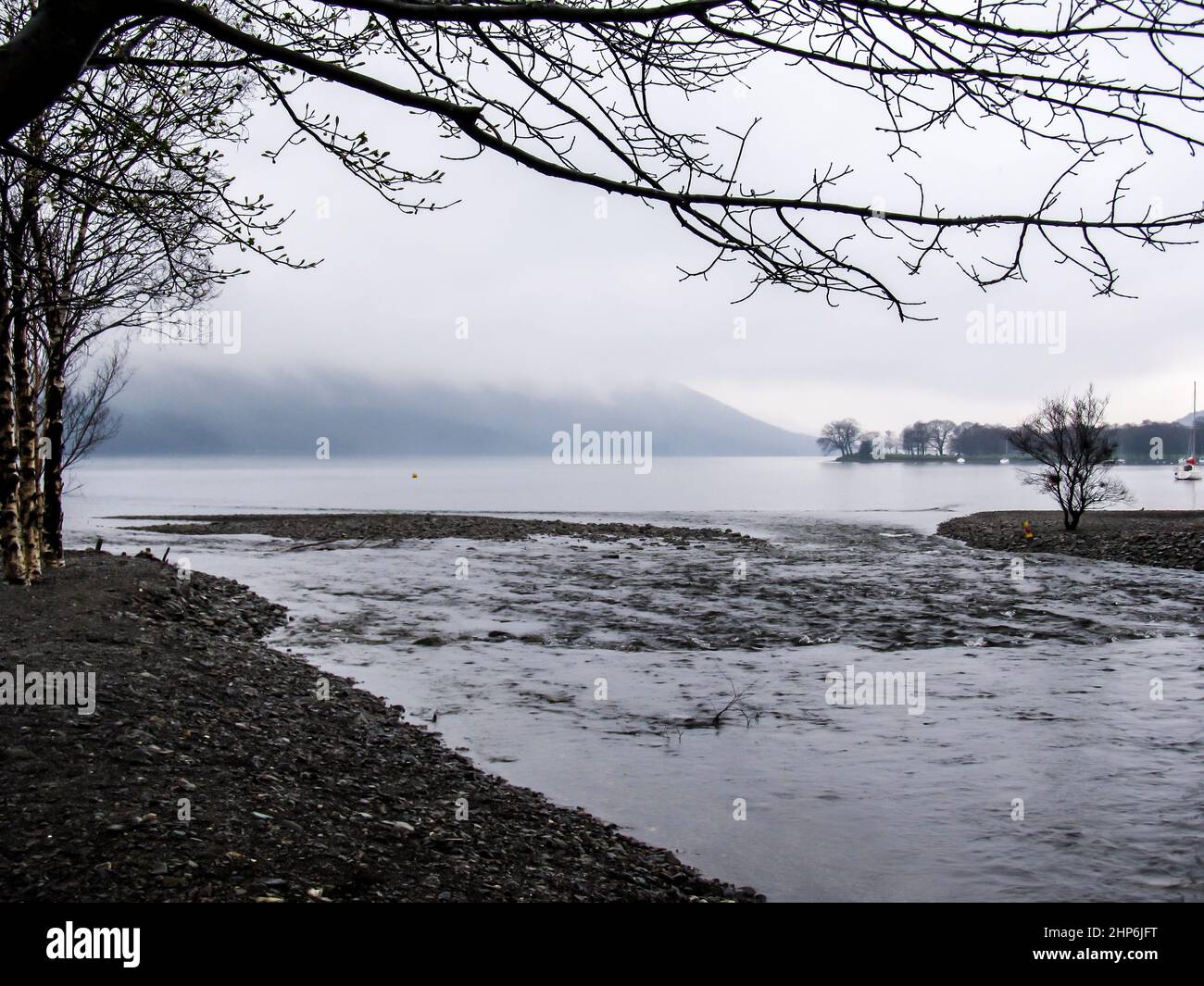 Ein kleiner Bach, der in das Wasser von Coniston fließt, wobei die Spitze der Berge im Hintergrund von Nebel umhüllt ist Stockfoto