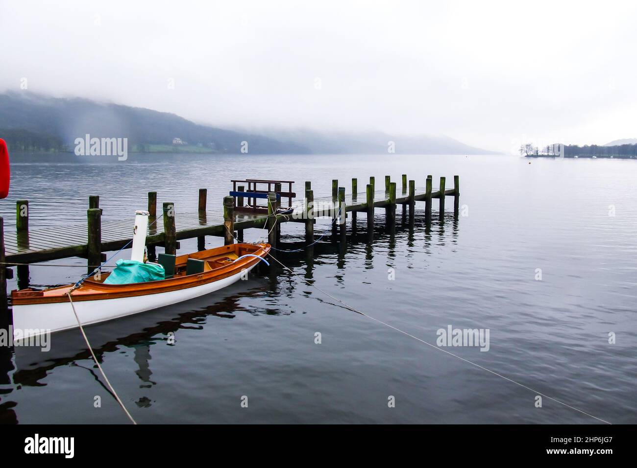 An einem nebligen Tag vertäute ein Boot neben einem Pier, das sich bis nach Coniston Water, Großbritannien, erstreckt Stockfoto