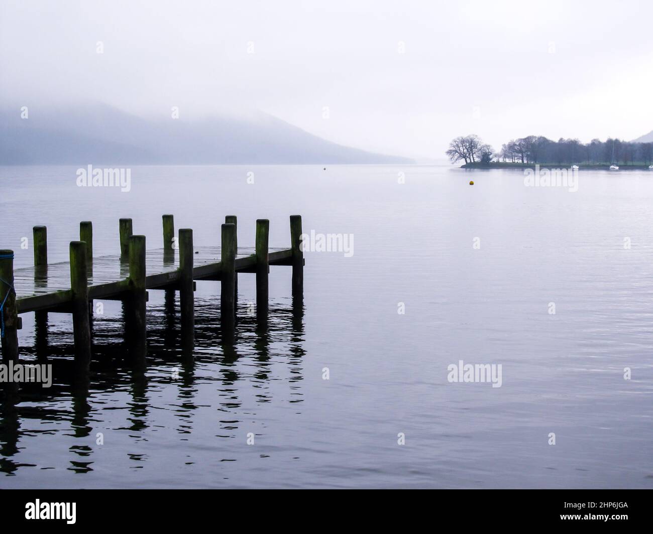 Ein Pier, der sich an einem nebligen und regnerischen Tag bis nach Coniston Water, Großbritannien, erstreckt, während der alte Mann von Coniston im Hintergrund durch Nebel verdeckt wird Stockfoto