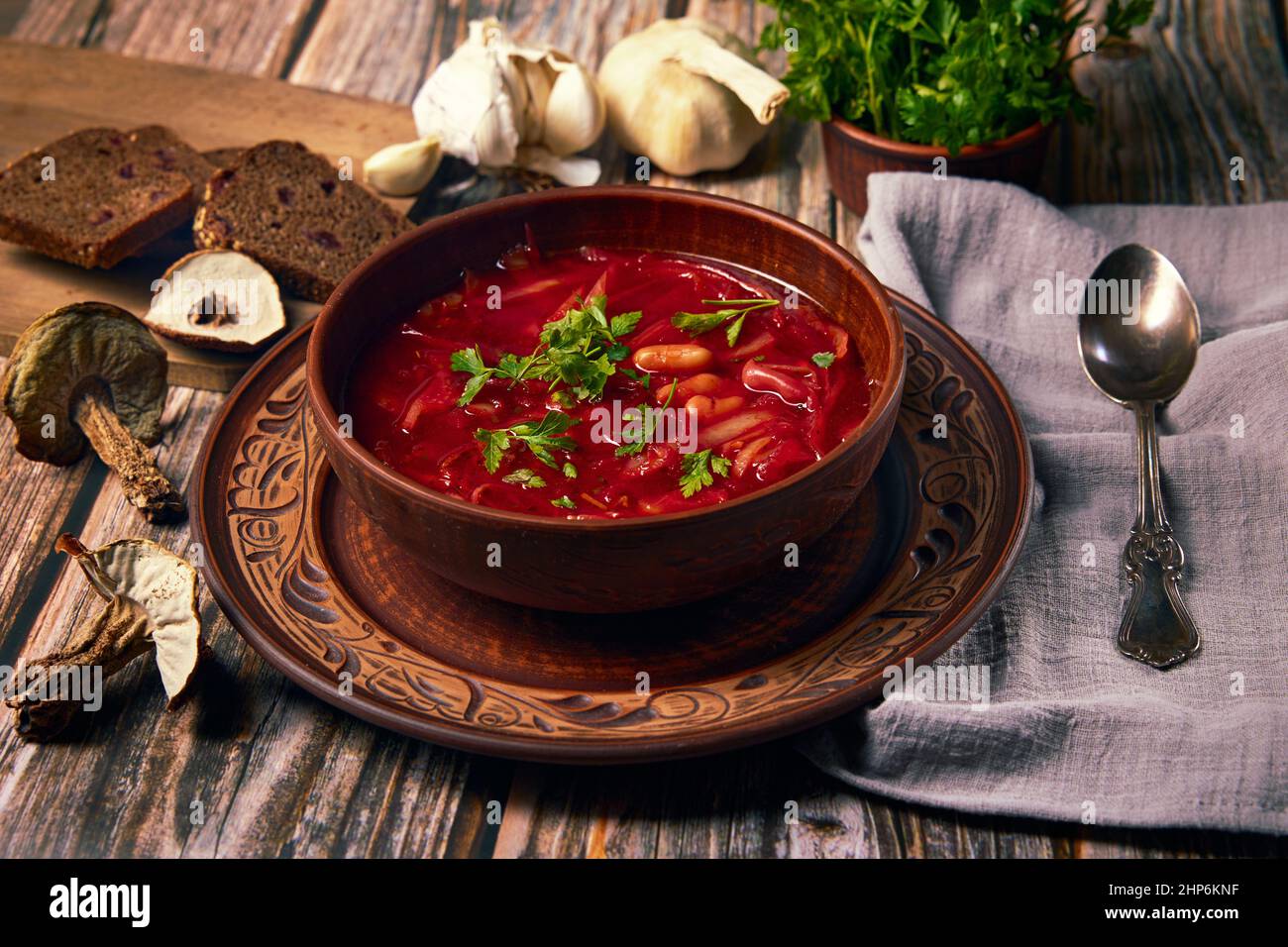 Ukrainische Zisine. Borsch ist eine ukrainische Suppe mit Steinpilzen, Kohl, Rote Beete, Zwiebeln, Karotten und Bohnen in Keramikplatte aus ökologischem Rot Stockfoto