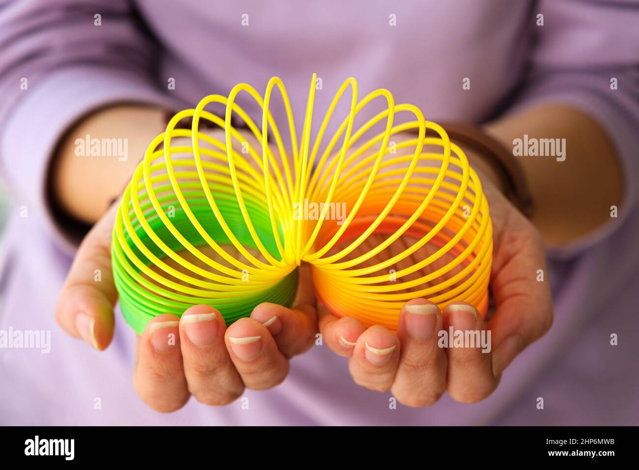 Frau, die mit dem magischen Frühlingsspielzeug der neunziger Jahre spielt, dehnbarer Regenbogen aus Kunststoff in der Hand, um Stress zu lindern oder zu reduzieren. Junge Frau mit Unterhaltungsidee. Stockfoto