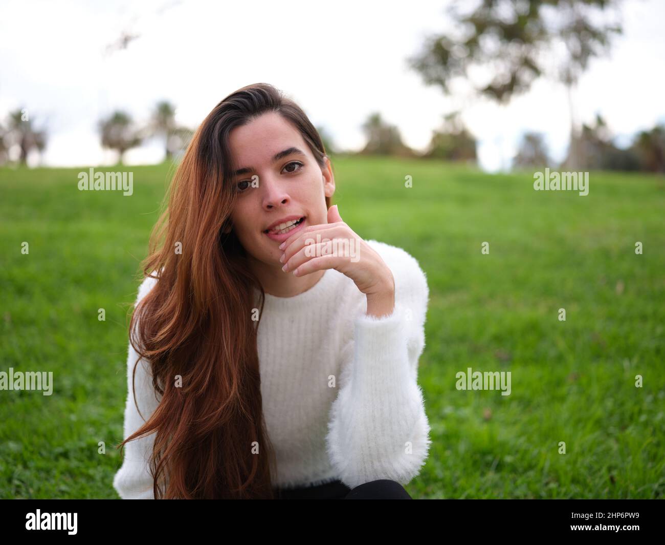 Eine wütende junge Frau im Park, die mit der Hand auf dem Kinn auf die Kamera schaut Stockfoto