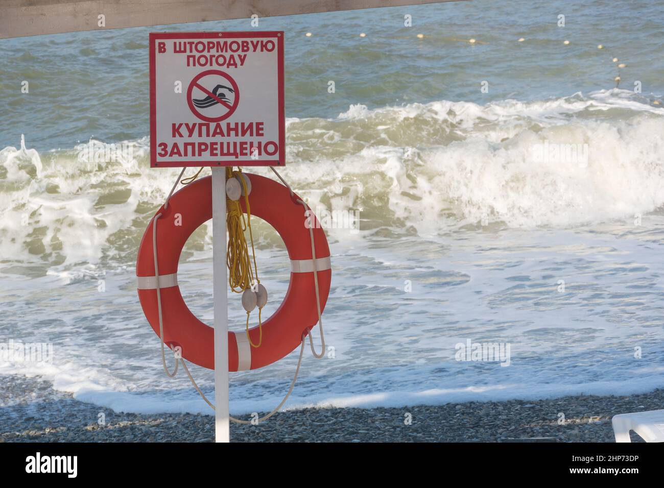 Schild mit der Aufschrift auf Russisch „bei stürmischem Wetter ist es verboten zu schwimmen“ vor dem Hintergrund großer Wellen und Rettungsboje. Verbotene Zone auf dem Stockfoto