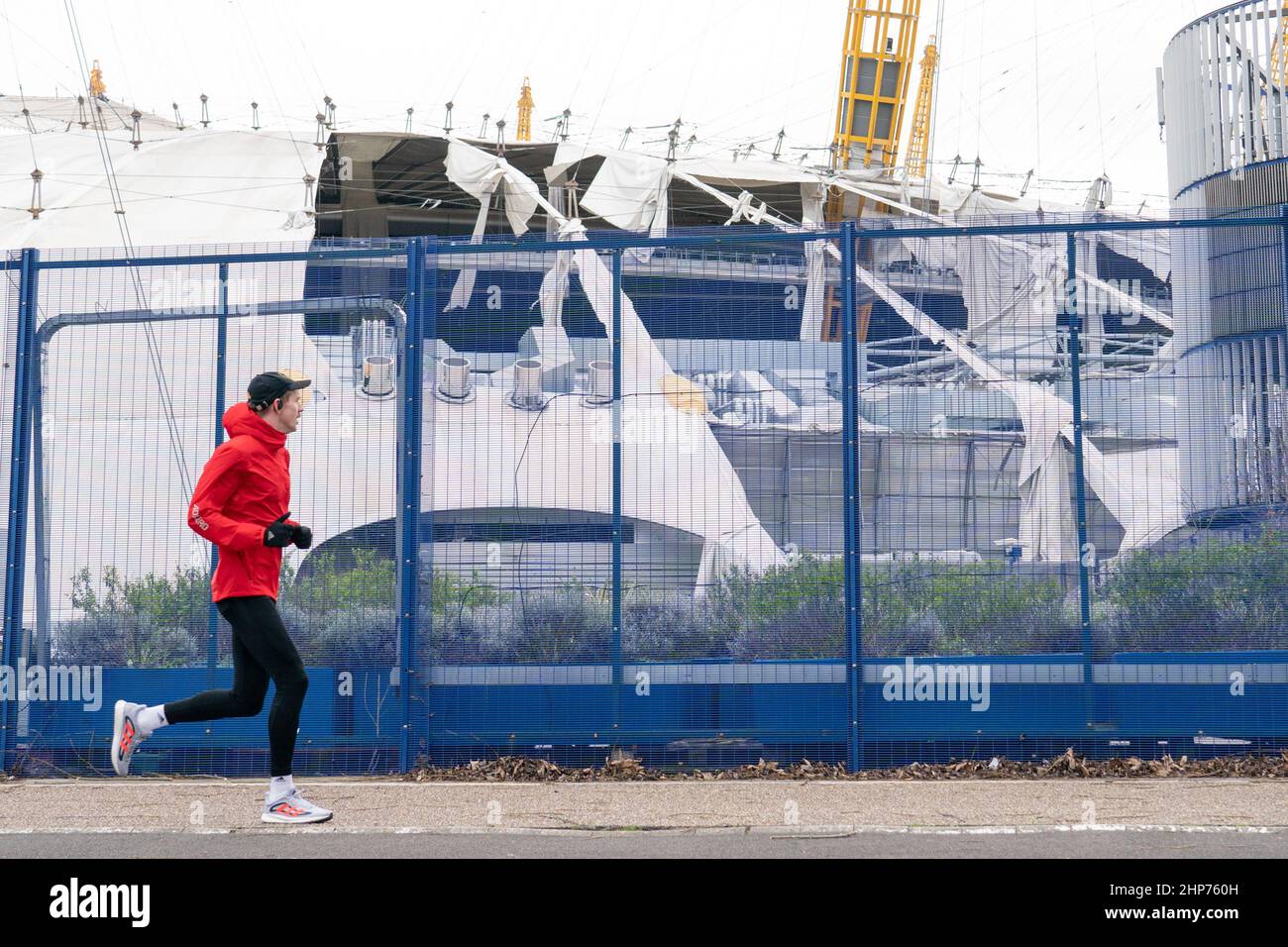 Ein Läufer kommt an der O2 Arena in London vorbei, nachdem Teile seines Dachs bei starken Winden abgerissen wurden, als der Sturm Eunice anschlug. Eine große Säuberung wird beginnen, nachdem Sturm Eunice Schäden, Störungen und rekordverdächtige Windböen in Großbritannien und Irland verursacht hat, die zum Tod von mindestens vier Menschen führen. Bilddatum: Samstag, 19. Februar 2022. Stockfoto