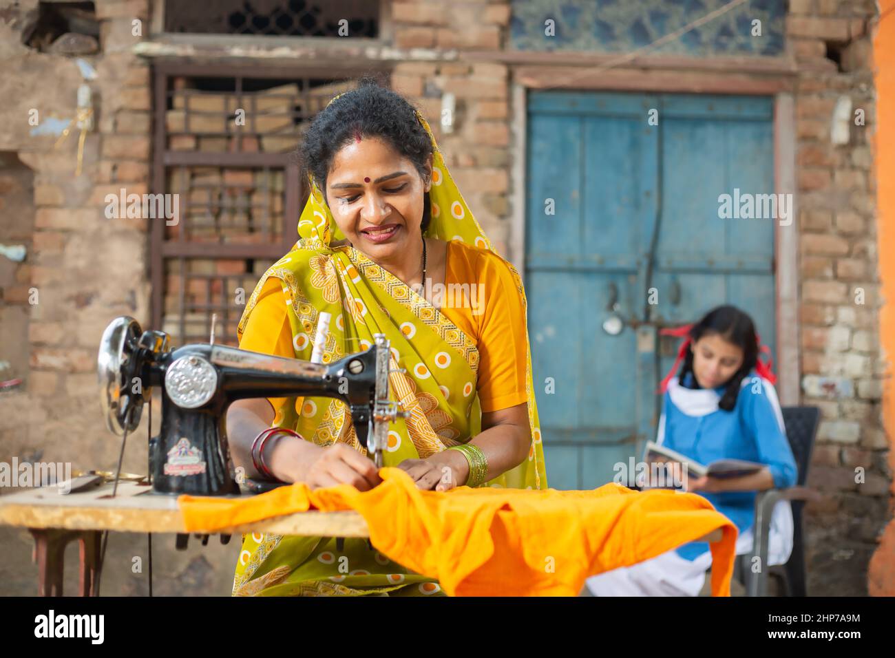 Ländliche indische Frau, die Nähmaschine benutzt, während ihre junge Tochter hinter ihr studiert. Stockfoto