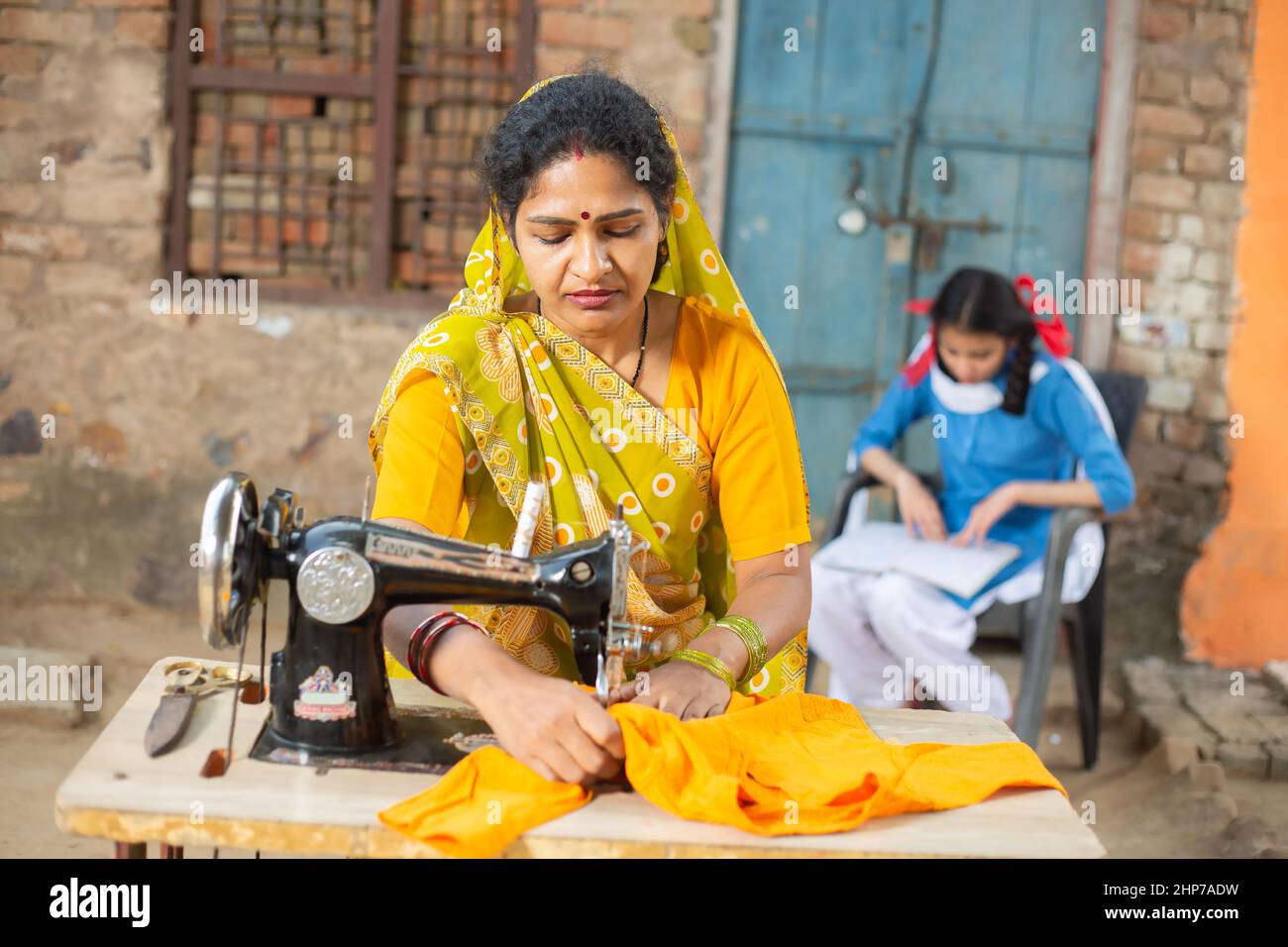 Ländliche indische Frau, die Nähmaschine benutzt, während ihre junge Tochter hinter ihr studiert. Stockfoto