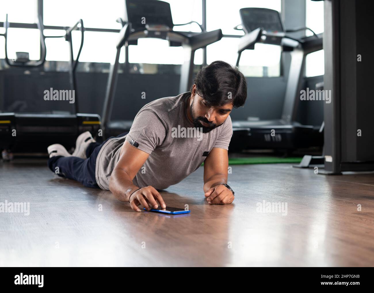 Junger Mann, der Liegestütze macht, indem er im Fitnessstudio einen Timer auf dem Mobiltelefon einstellt - Konzept von Muskel- oder Bodybuilding, Kalorienverfolgung und Technologie. Stockfoto
