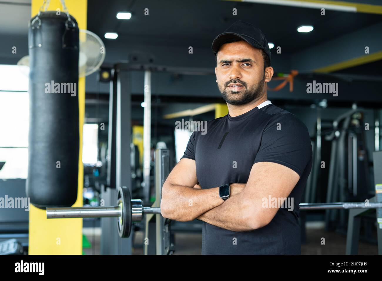 Porträtaufnahme eines Sporttrainers oder Trainers, der mit gekreuzten Armen in der Turnhalle steht, indem er die Kamera betrachtet – Konzept des Inhabers eines kleinen Unternehmens, des Selbständigen und Stockfoto
