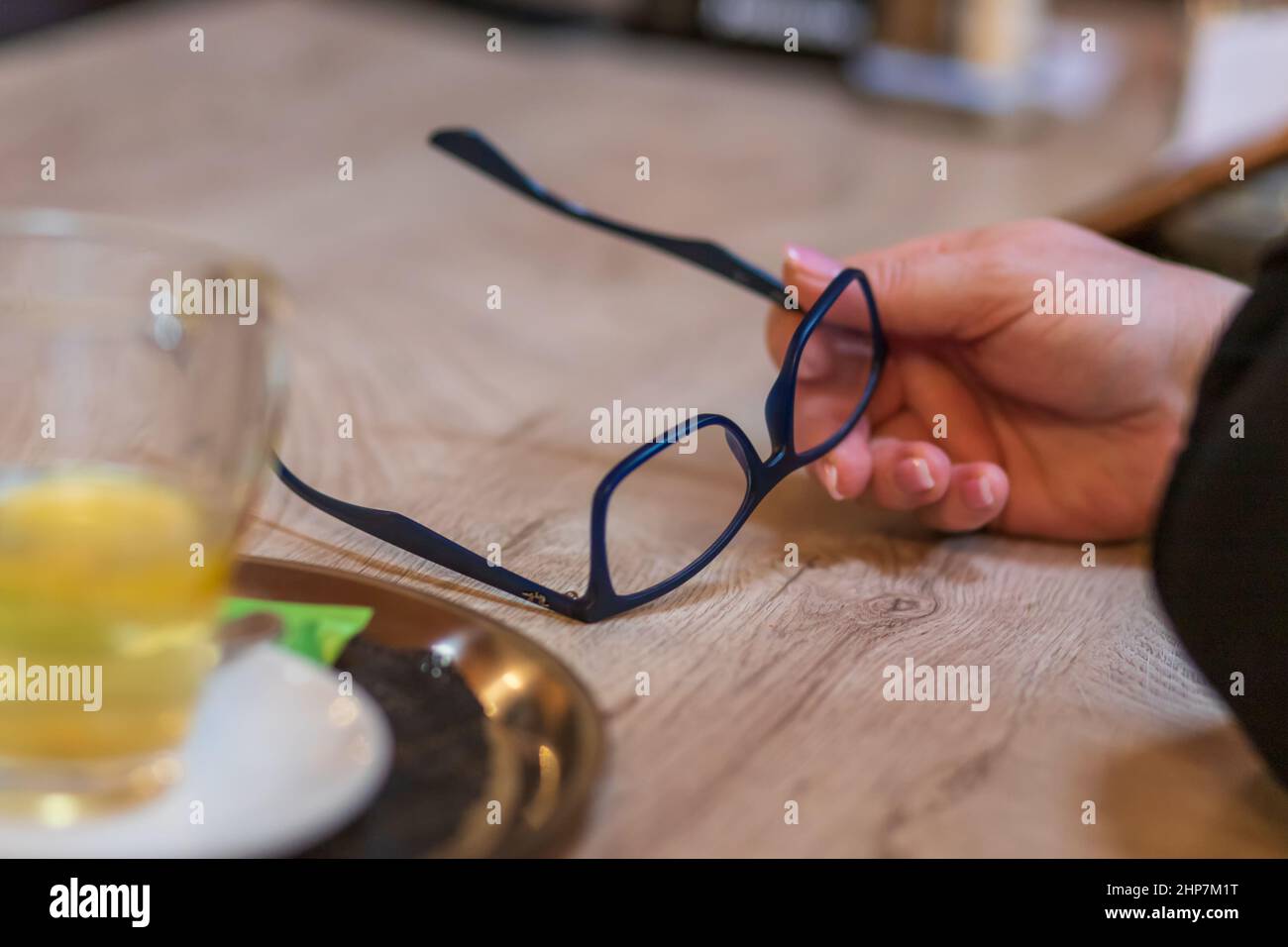 Die Frauenhand hält eine Brille und wird auf den Tisch gelegt. Stockfoto