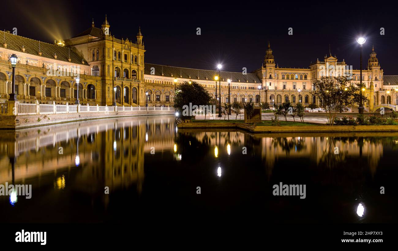 Spanish Square: Panoramablick auf das beleuchtete halbrunde Backsteingebäude des Spanish Square bei Nacht, das sich in seinem Miniaturkanal widerspiegelt. Sevilla, Spanien. Stockfoto
