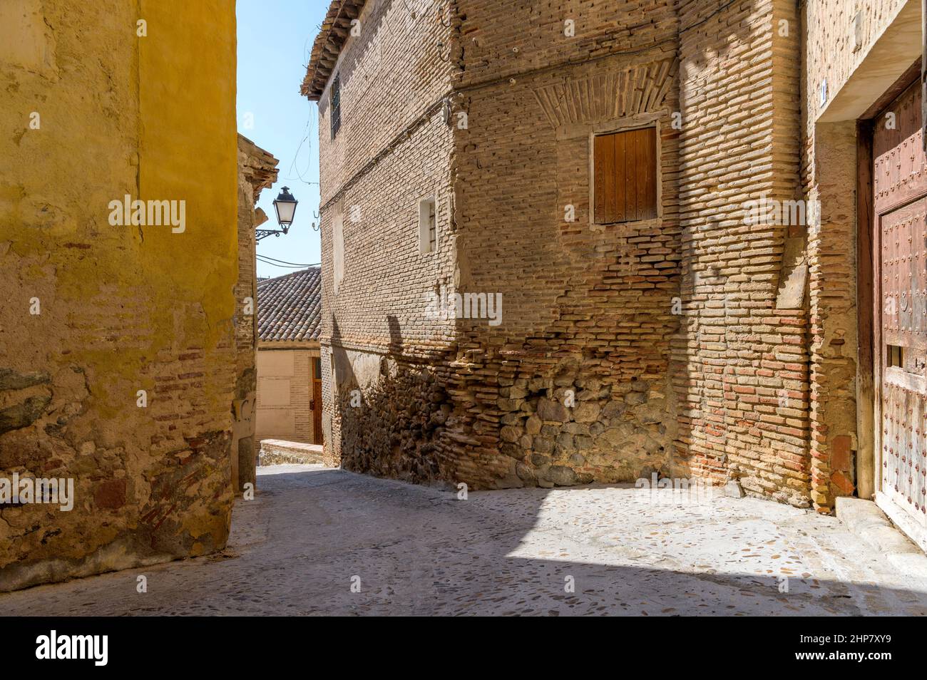 Old Street - in der historischen Stadt Toledo, Spanien, scheint am Nachmittag in einer engen Straße, die von alten Backstein- und Steingebäuden umgeben ist, helles Sonnenlicht. Stockfoto