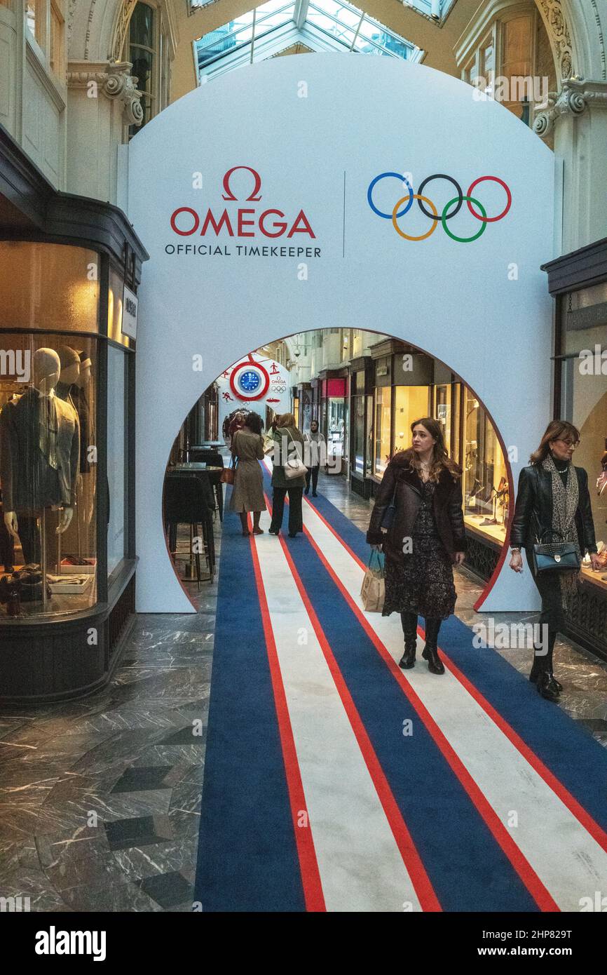 Die Käufer passieren einen Bogen von Omega, der für die Olympischen Winterspiele, die Royal Arcade, Old Bond Street, London, wirbt Stockfoto
