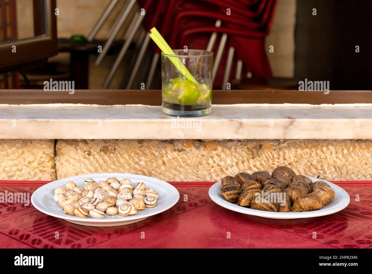 Zwei Teller mit verschiedenen Schnecken und einem Glas Caipirinha Stockfoto