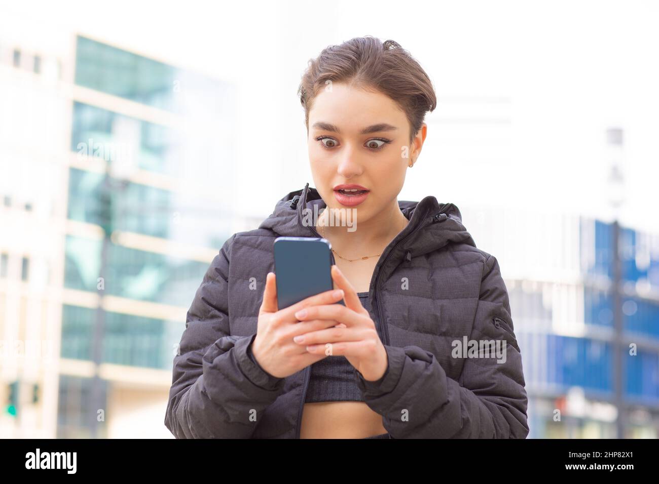 Porträt einer staunenden Frau, die ihr Handy auf einem Stadthintergrund ansieht Stockfoto