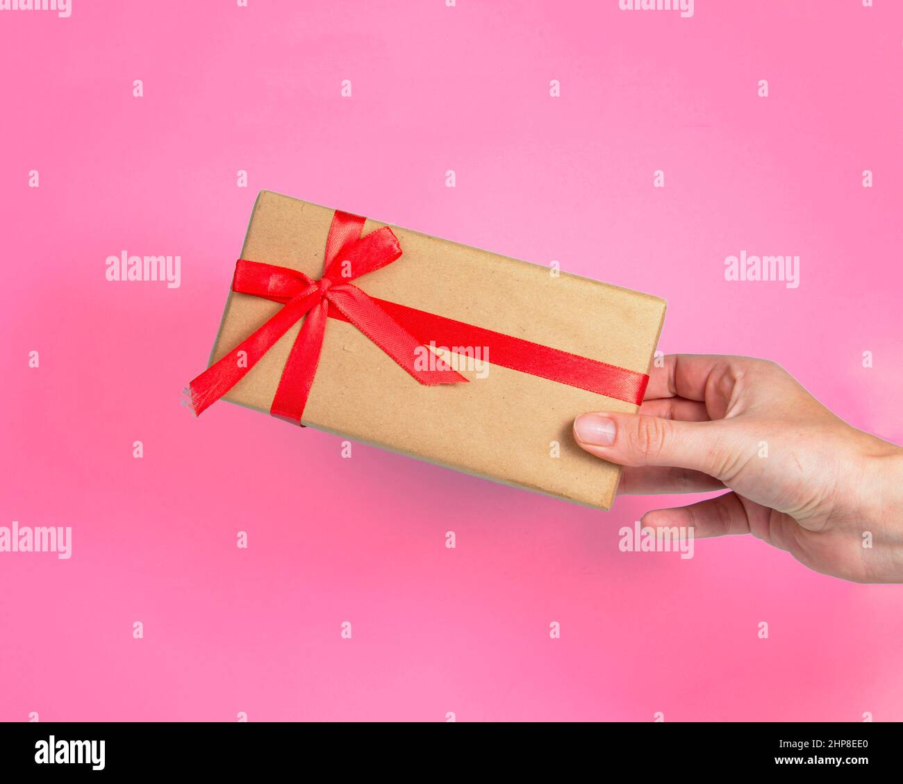 Geschenkbox Bastelpapier mit roter Schleife in der Hand auf rosa Hintergrund Stockfoto