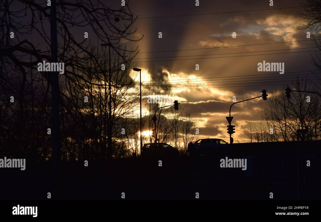 An einer Ampel brechen Sonnenstrahlen durch den Abendhimmel Stockfoto