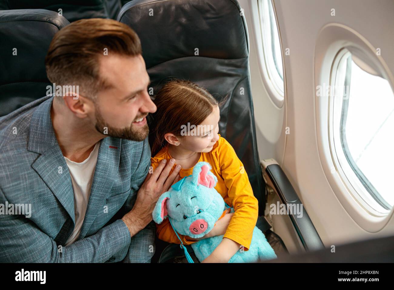 Fröhlicher Mann und kleines Mädchen, die aus dem Fenster im Flugzeug schauen Stockfoto