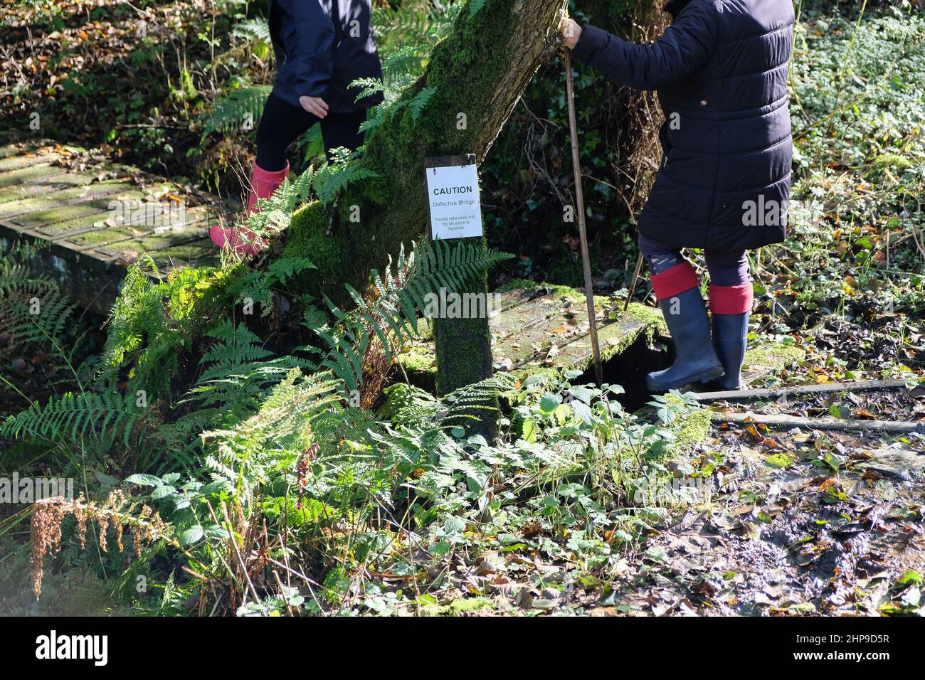 Ein Schild warnt vor einer kaputten Brücke, über die 2 Frauen in wellington-Stiefeln hindurchfahren Stockfoto