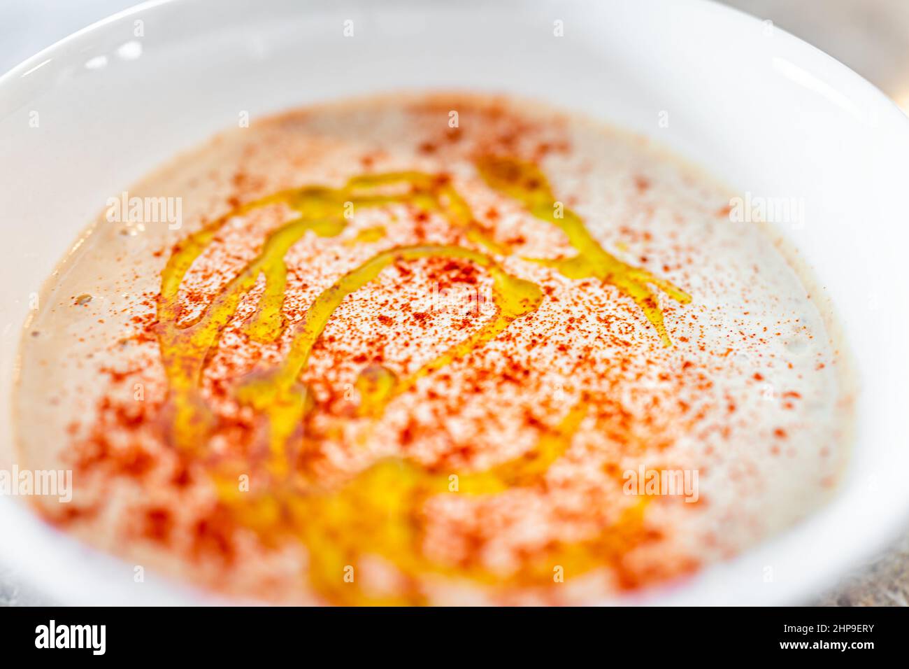Oben Ansicht Makro Nahaufnahme von Hummus verteilt hausgemachte mit Kichererbsen Paprika Harissa Gewürze und Knoblauch in einer weißen Schüssel mit beträufigem Olivenöl auf der Oberseite Stockfoto