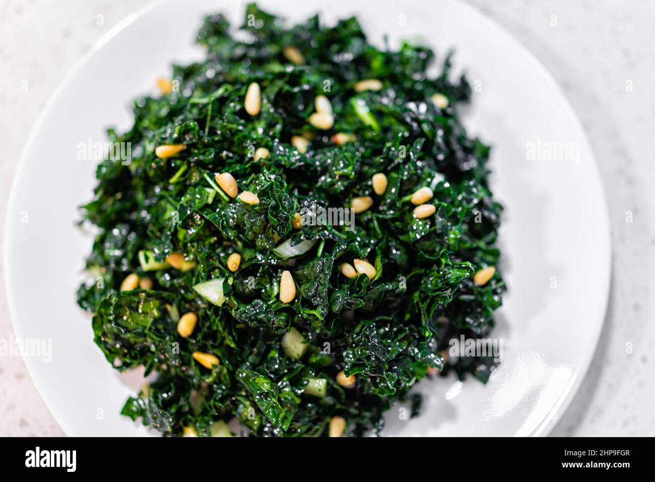 Flache Nahaufnahme Textur Ansicht von grünem Grünkohl veganen vegetarischen Salat auf weißem Teller mit Pinienkernen und Olivenöl Hintergrund Stockfoto