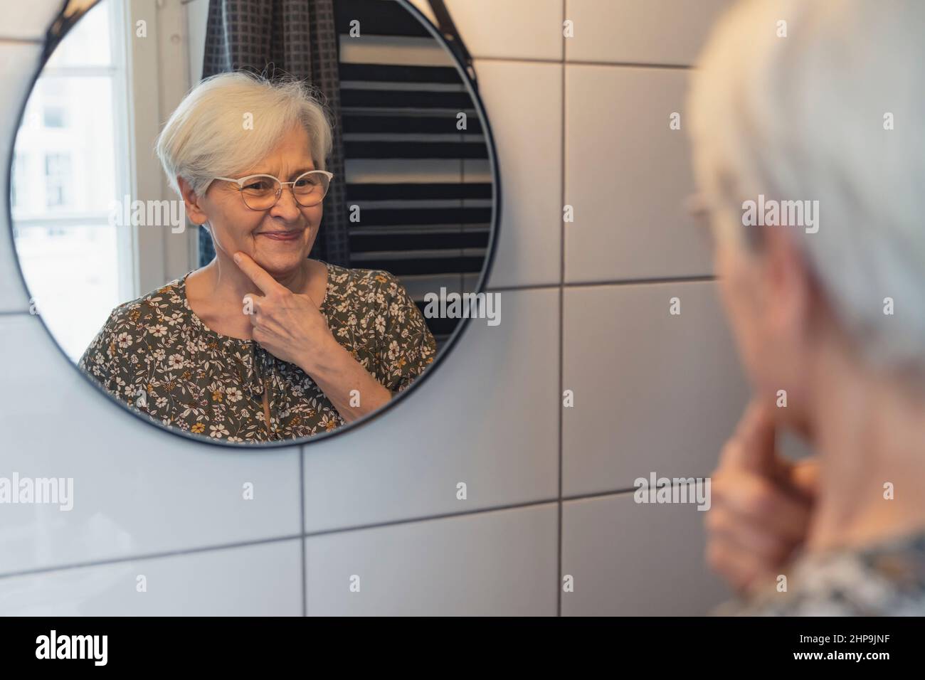 Eine kaukasische Rentnerin zeigt auf ihre alte, faltige Haut im Spiegel. Hochwertige Fotos Stockfoto