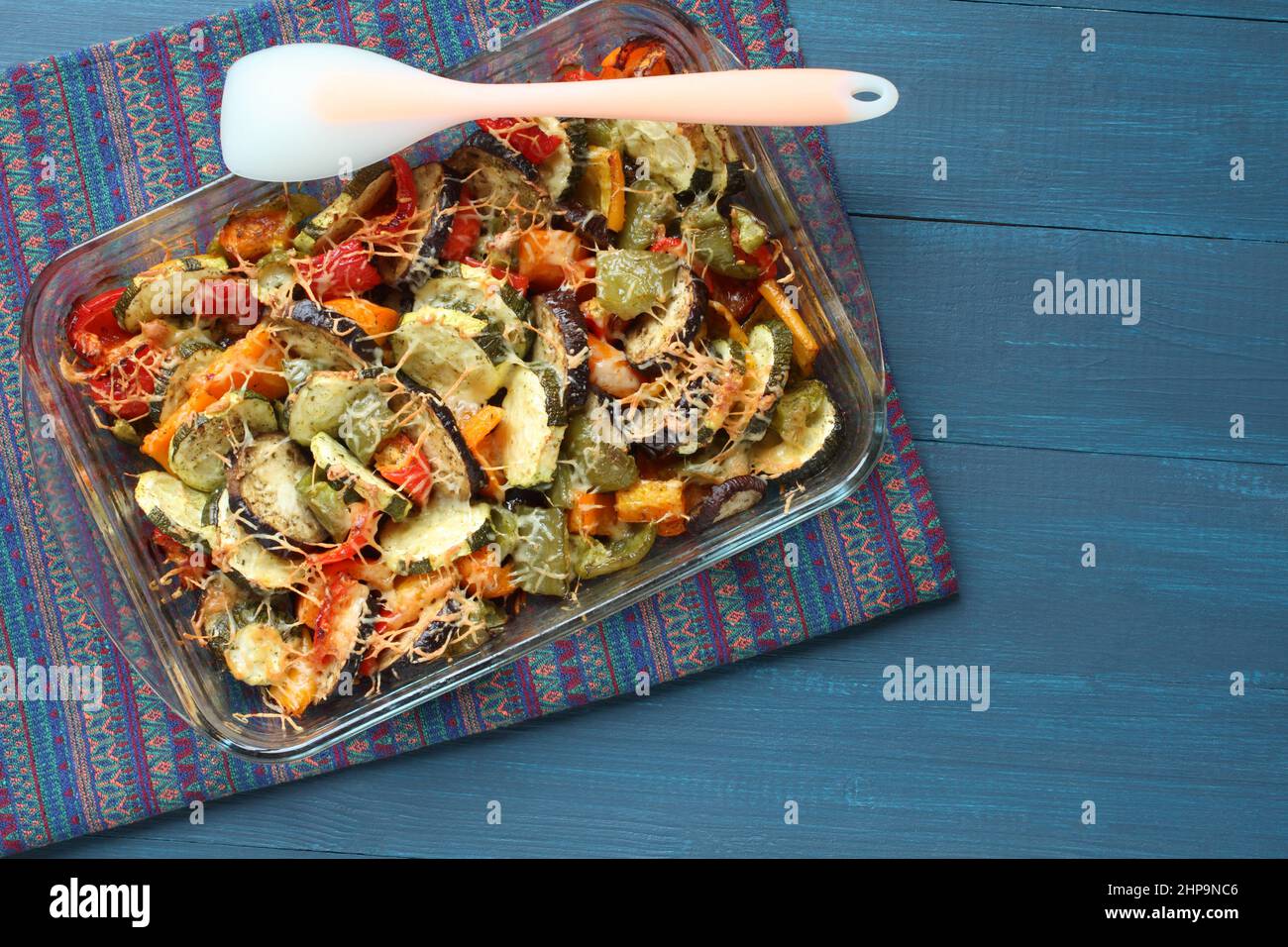 Gemüseauflauf mit Zucchini, Paprika, Auberginen und Käse, in Glasform gebacken, der auf einem blauen Holztisch steht. Blick von oben. Nahaufnahme. Stockfoto