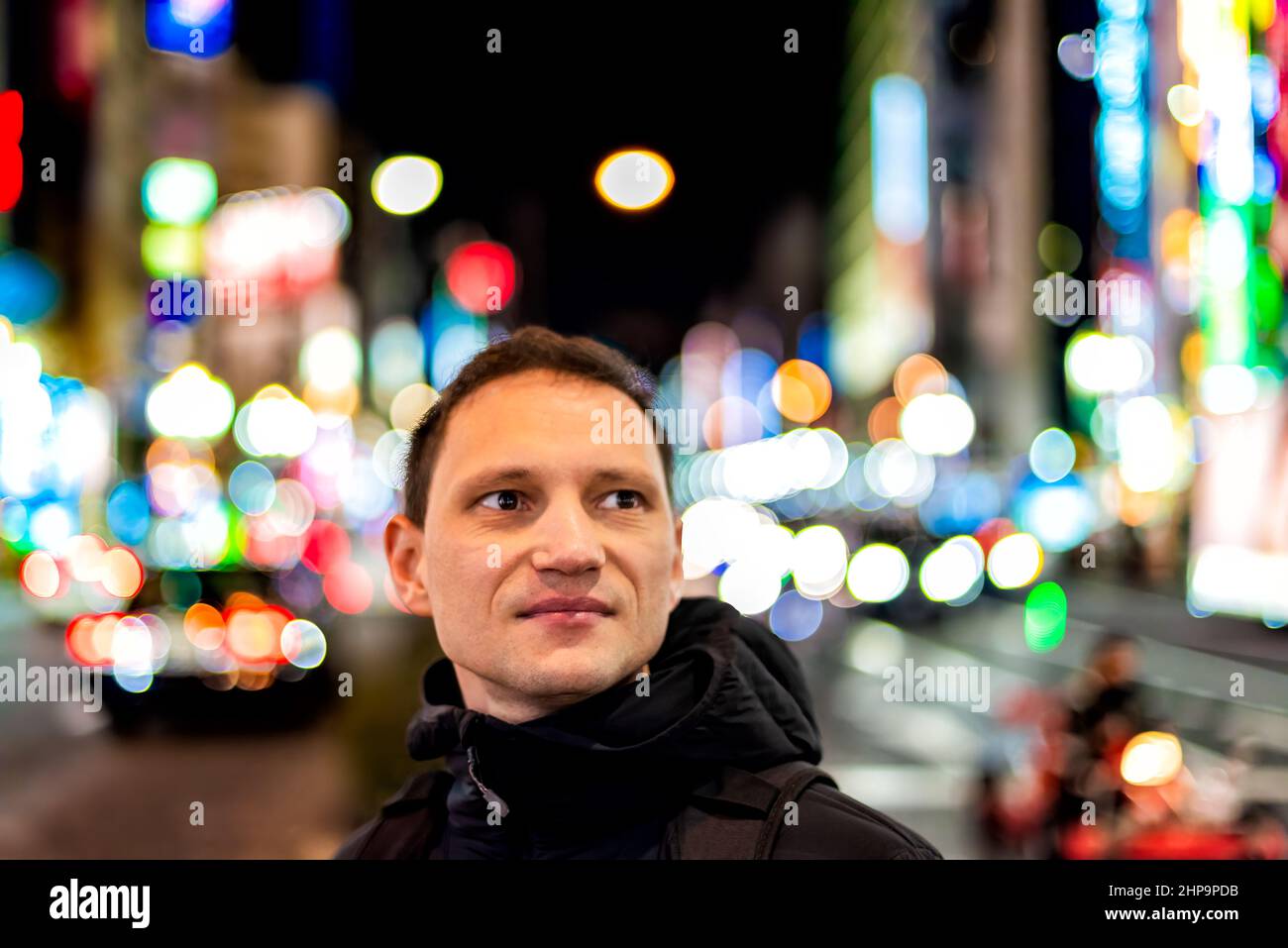 Tokio, Japan Shinjuku in der Innenstadt bei Nacht mit einem Porträt eines jungen Mannes, der das Nachtleben mit verschwommenem Hintergrund aus buntem Neon-Bokeh-Licht betrachtet Stockfoto