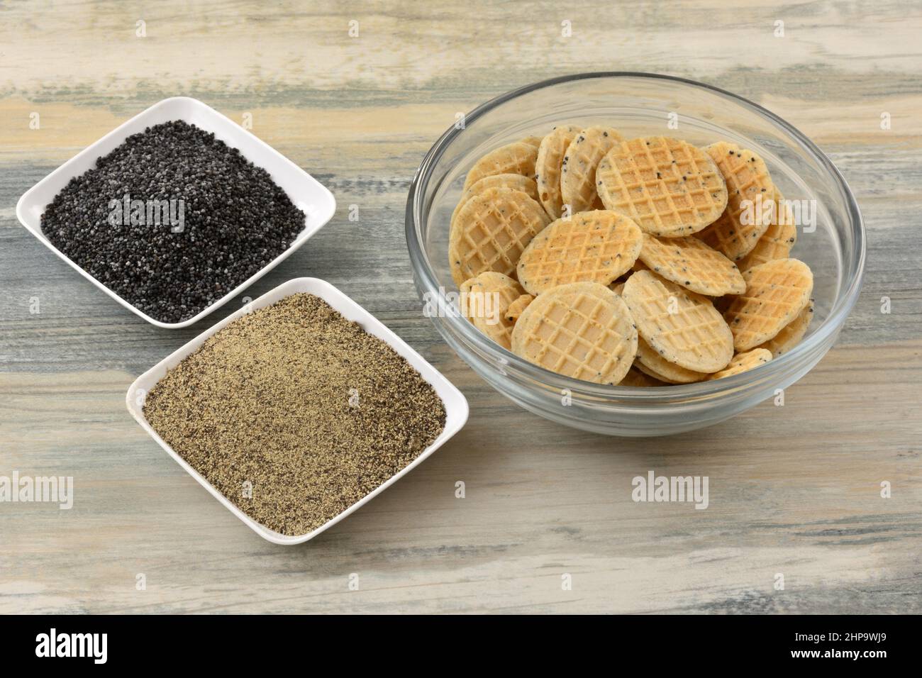 Schwarzer Pfeffer und Mohn-Waffelplätzchen in Glasschüssel mit Mohn-Samen und schwarzem Pfeffer auf zwei kleinen Zutatengerichten Stockfoto