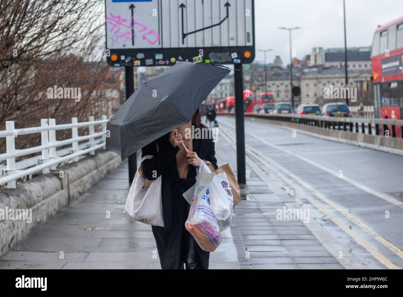 LONDON, 19 2022. FEBRUAR, Fußgänger laufen mit einem Regenschirm über die Waterloo Bridge, während das regnerische Wetter nach dem Sturm Eunice anhält. Das Met Office veröffentlichte zwei seltene rote Warnungen, da Großbritannien während des schlimmsten Sturms seit 30 Jahren von Regen, Schnee und rekordverdächtigen 122 mph starken Winden getroffen wurde. Stockfoto