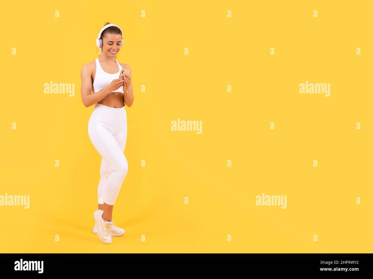 Sportfrau mit Kopfhörer und Smartphone auf gelbem Hintergrund. Platz kopieren Stockfoto