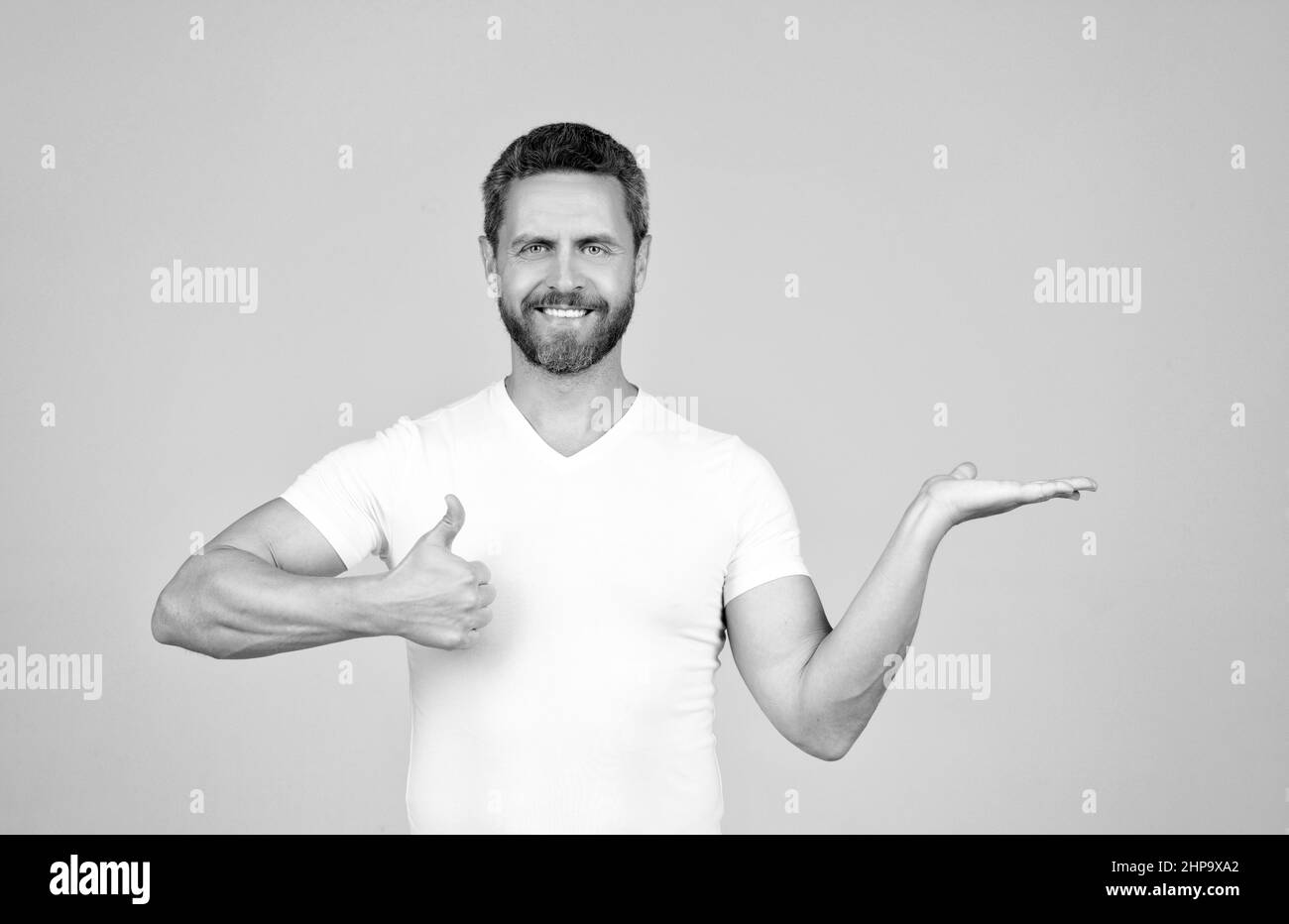 Das beste Produkt präsentieren. Glücklicher Mann zeigt die offene Hand und zeigt den Daumen nach oben. Produktpräsentation Stockfoto