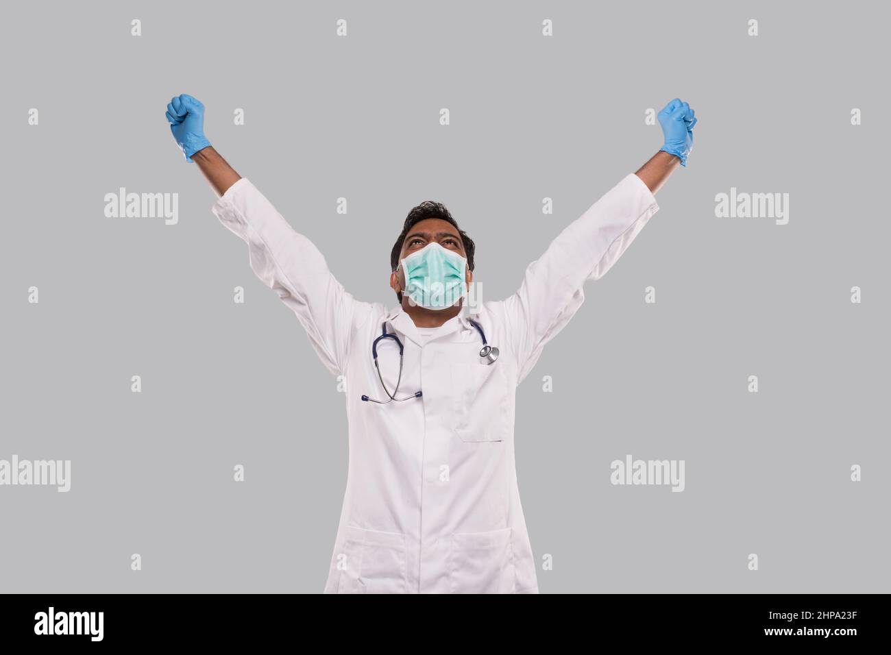 Arzt begeistert Hände hoch Erfolg zu feiern tragen medizinische Maske und Handschuhe isoliert. Indischer Mann Arzt Glücklich Stockfoto