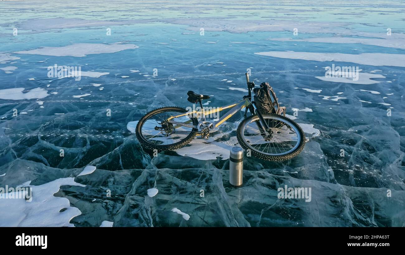 Mann und Fahrrad auf Eis. Er schaut auf das schöne Eis in den Rissen. Blick auf die erste Person auf dem Fahrrad. In der Nähe befindet sich eine Thermoskanne und ein Fahrradrucksack. Eis des Th Stockfoto