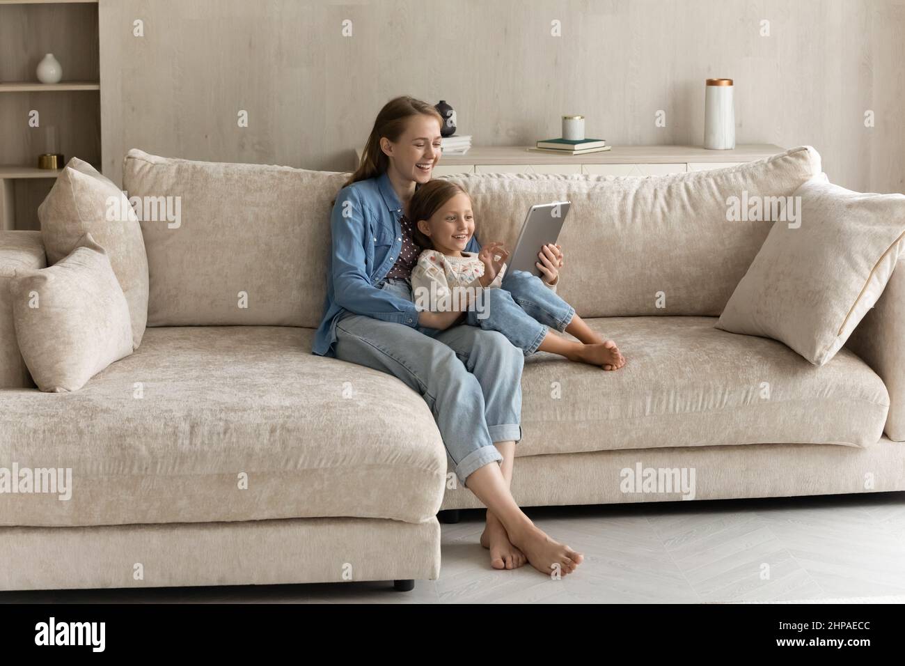Glückliche junge Mutter umarmt süße Tochter Kind auf bequeme Couch Stockfoto