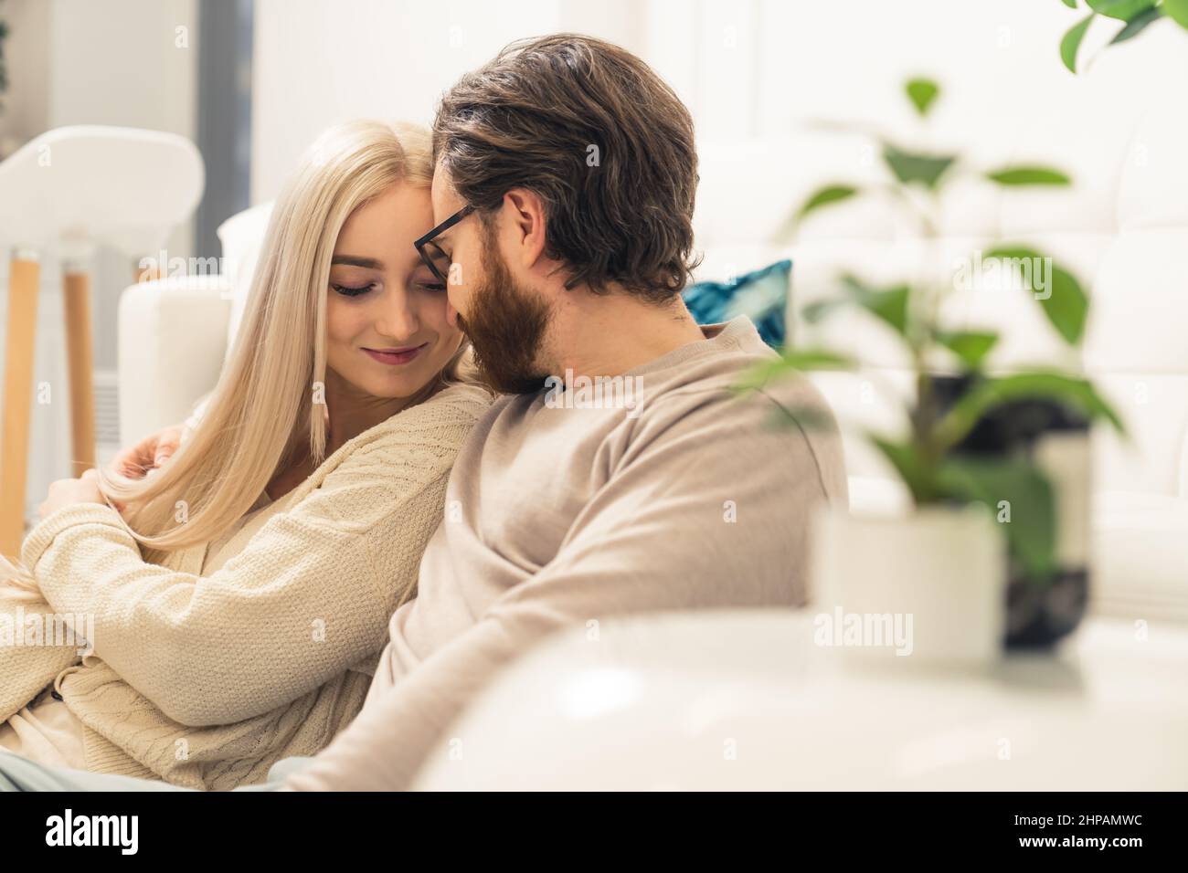 Zärtliche kaukasische junge Ehegatten kuscheln und flüstern, während sie auf einem Sofa sitzen. Hochwertige Fotos Stockfoto