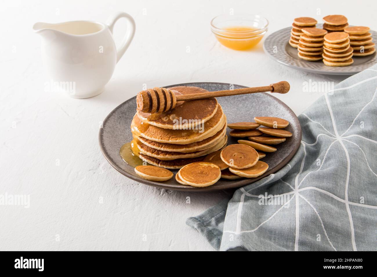 Hausgemachte Pfannkuchen und Mini-Pfannkuchen auf einem grauen Teller werden mit Honig serviert. Rahm oder Milch, eine Schüssel mit Honig, um den Geschmack zu verbessern Stockfoto