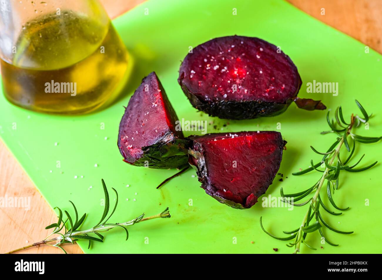 Drei gebackene Betroot-Stücke, Rosmarinzweig und ein Glas Olivenöl auf einem grünen Küchentafel auf dem Tisch. Stockfoto