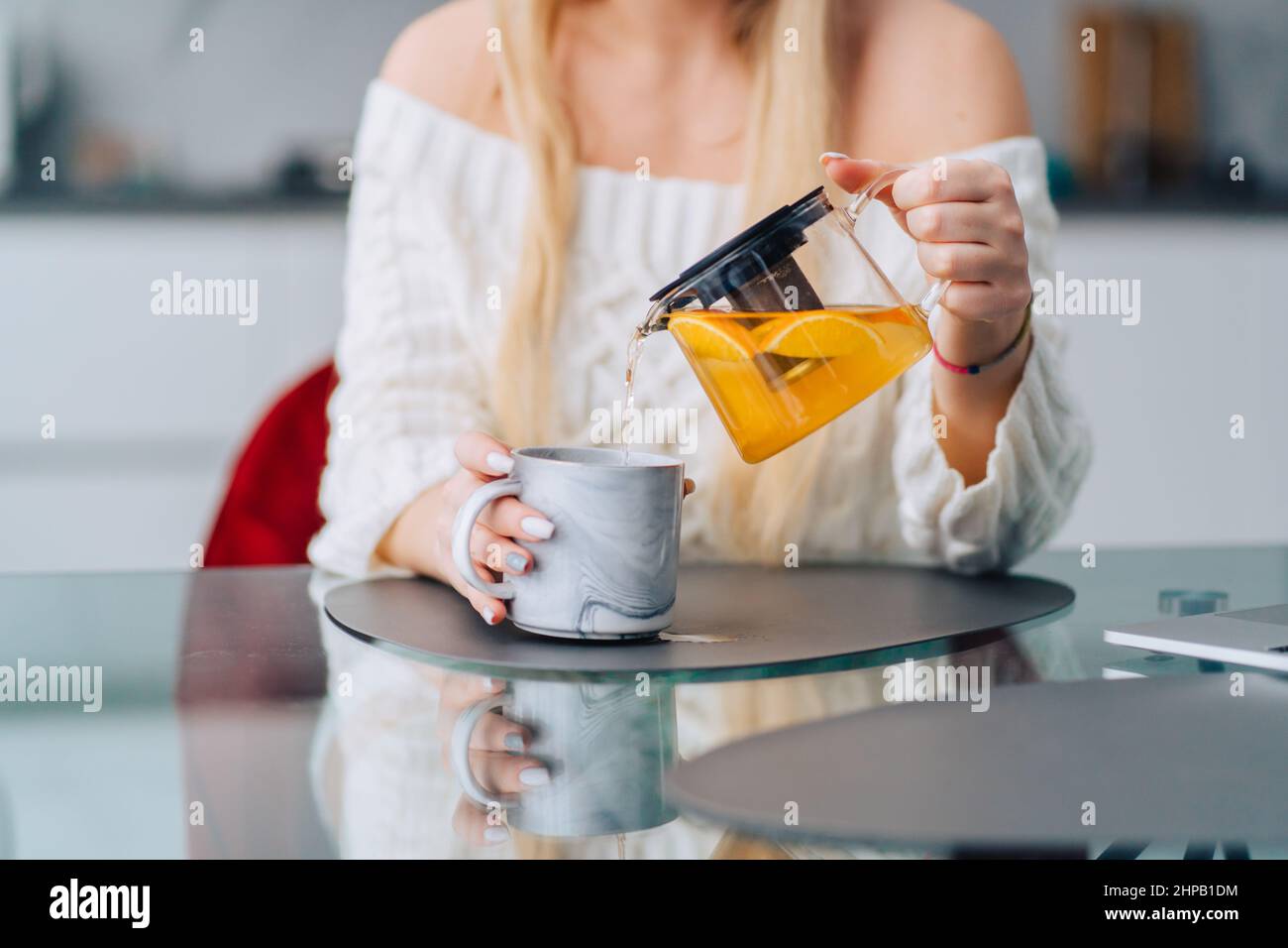 Blonde attraktive Frau Küche Gießen Zitrone Tee Teekannen. Vase mit Tischblumen Stockfoto