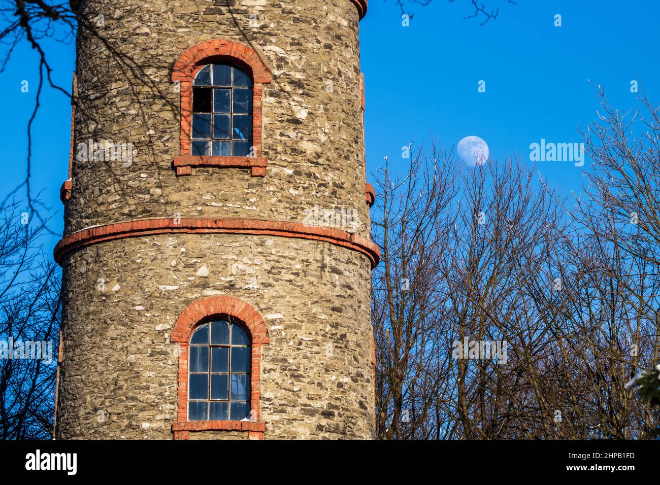 fenster in einem alten runden Ziegelturm vor Vollmond in blauem Himmel Stockfoto