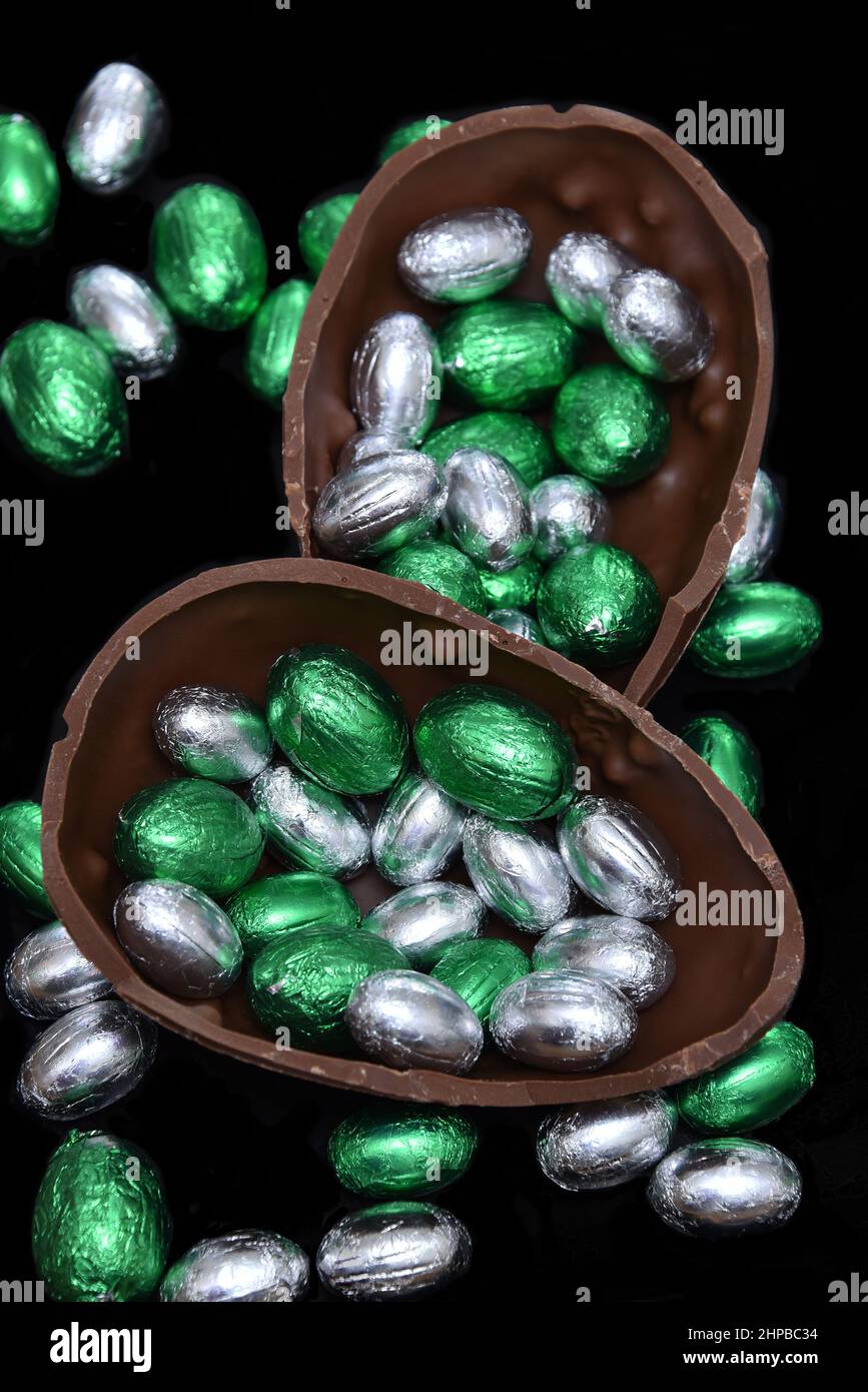 Bunte, in Folie verpackte Schokoladen-ostereier in Silber und Grün mit zwei Hälften eines großen braunen Milchschokoladeneier in der Mitte und Mini-Eiern. Stockfoto