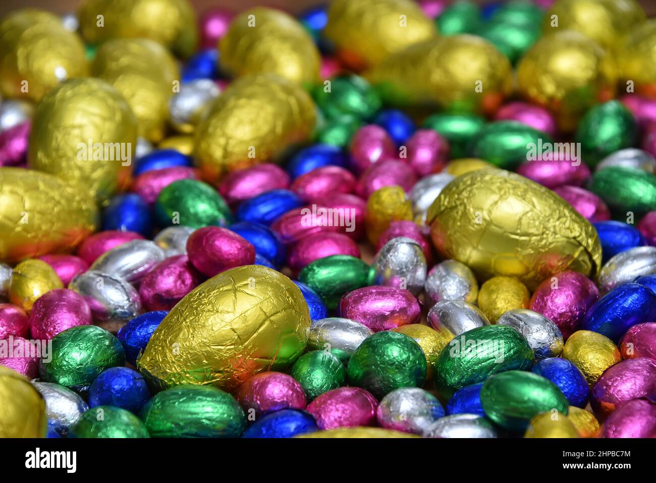 Kleine rosafarbene, blaue, grüne und silberne Schokoladen-ostereier mit größeren gelben Eiern auf hellem Holzgrund. Stockfoto