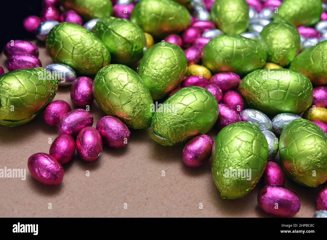 Kleine rosa, gelbe, grüne und silberne, in Folie gewickelte Ostereier aus Schokolade mit größeren lindgrünen Eiern vor einem hellen Holzhintergrund. Stockfoto