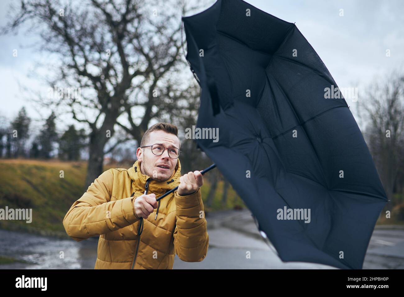 Mann hält gebrochenen Regenschirm bei starkem Wind während düsteren regnerischen Tag. Themen Wetter und Meteorologie. Stockfoto