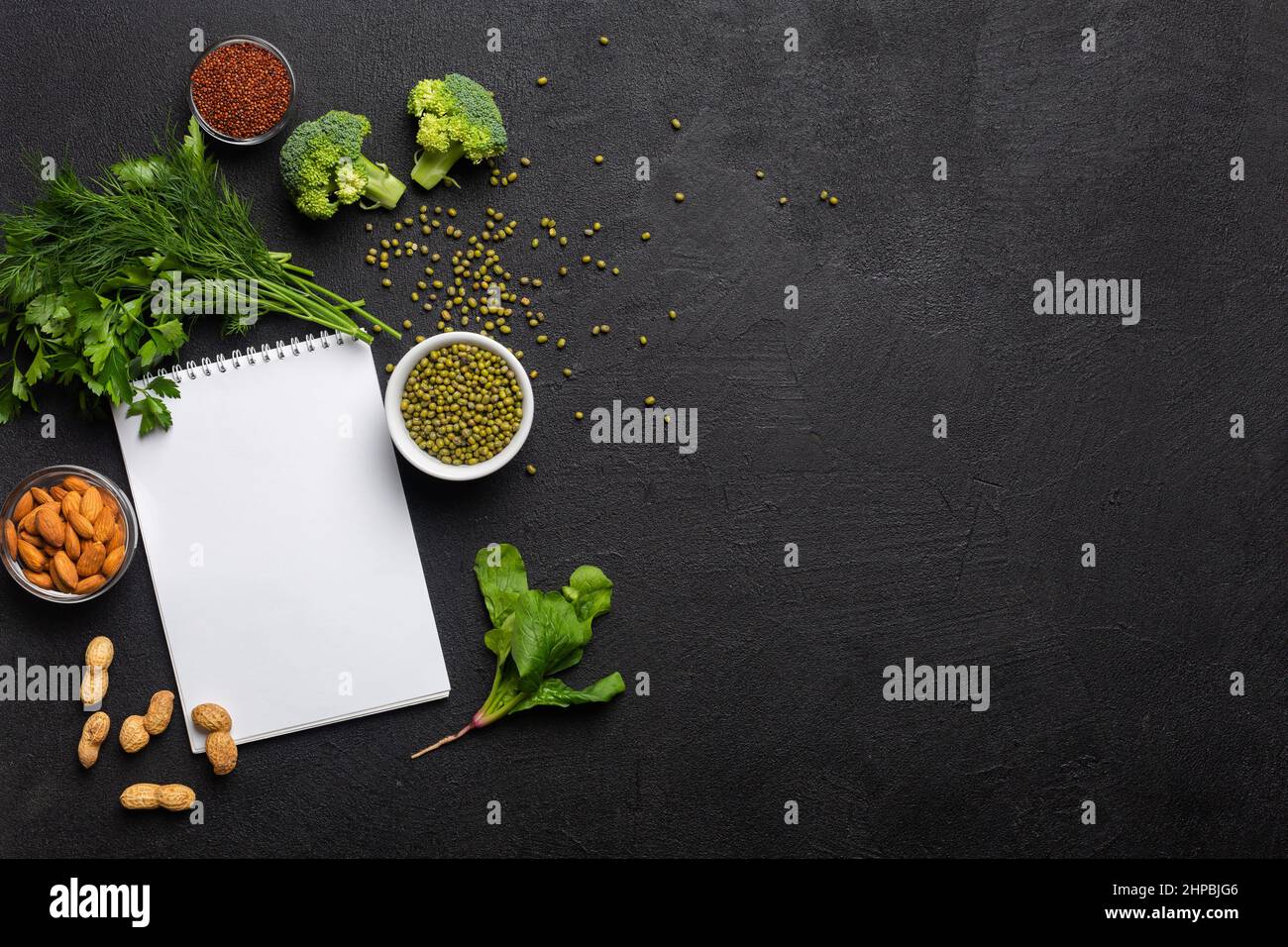 Eine Proteinquelle für Vegetarier. Gesunde, saubere Lebensmittel: grünpflanzen, Gemüse, Nüsse und Hülsenfrüchte Draufsicht auf schwarzem Hintergrund mit weißem Notizblock. Stockfoto