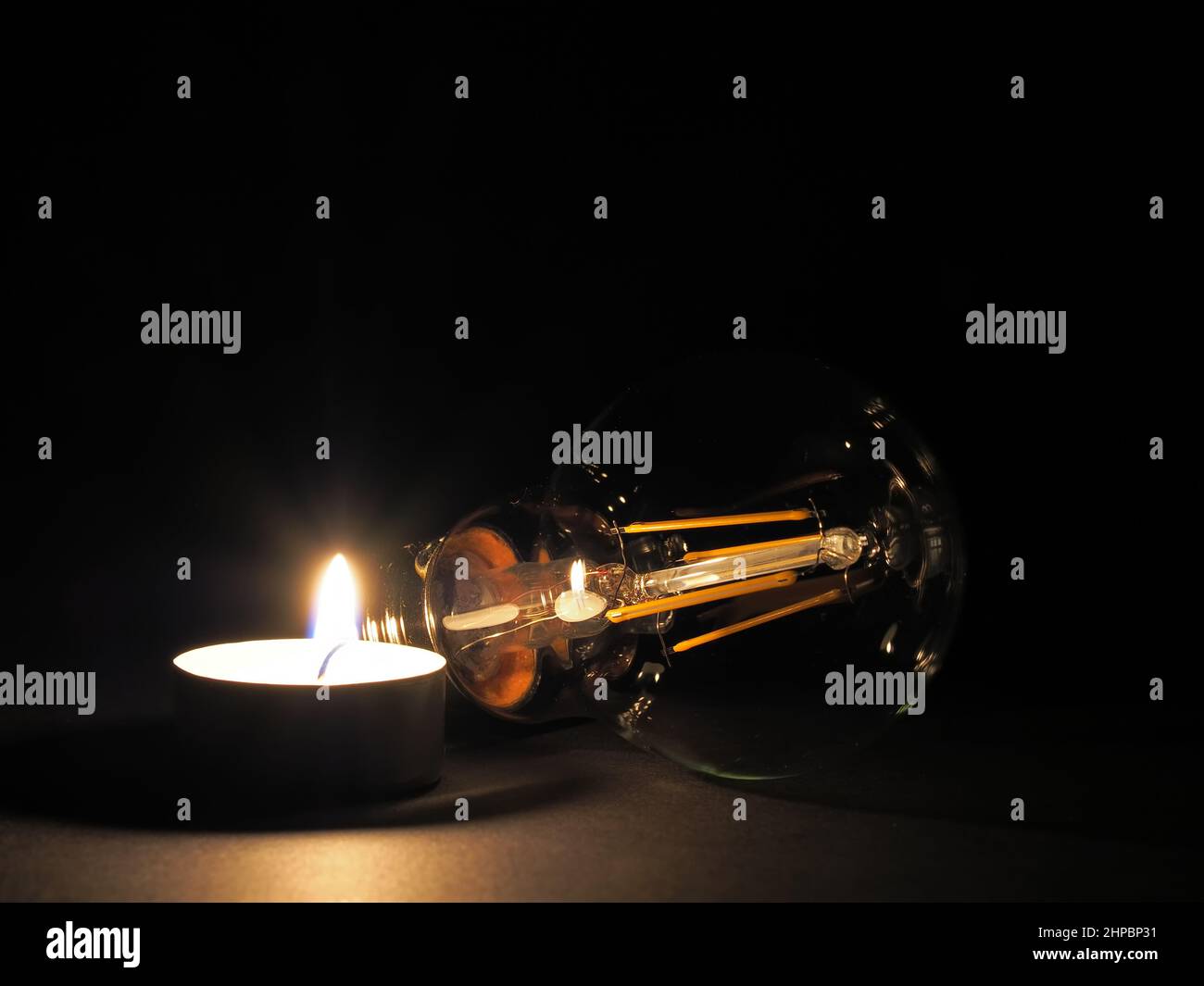 Kerze brennt neben einer Glühbirne. Konzept steigender Energiekosten, Armut und Energieknappheit Stockfoto