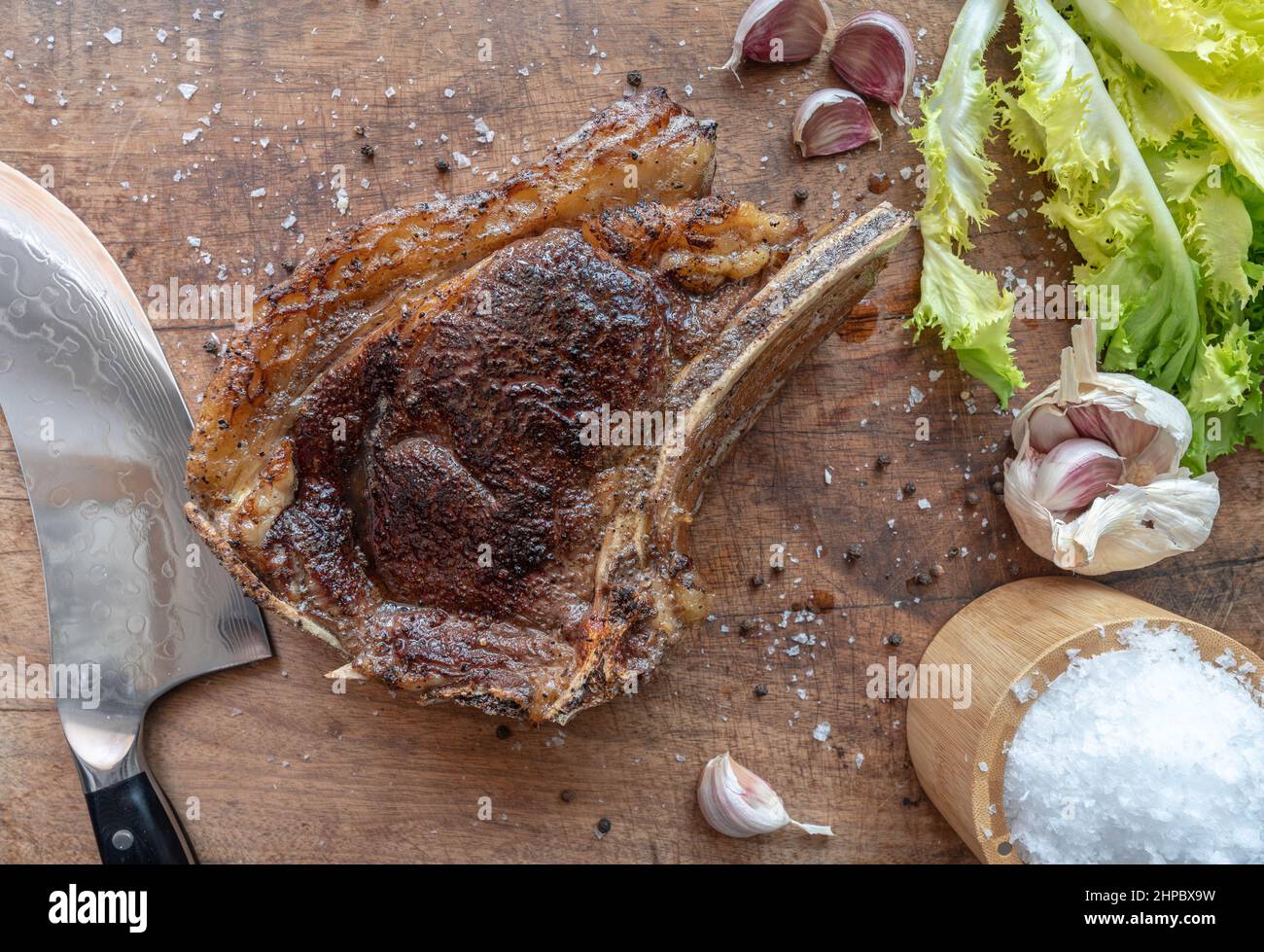 Sous Vide gekochtes mittelseltenes, trocken gereiftetes rubia Gallega Rindersteak mit Messer, Meersalzflocken, Knoblauch, Pfeffer und Salat auf einem Holzbrett Stockfoto